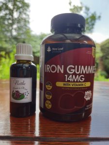 New Leaf Iron Gummies and our Nettle Tincture on a wooden table with a green outdoor background, used for iron deficiency support